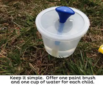 paint brush in container with water for outdoor art activity for preschool