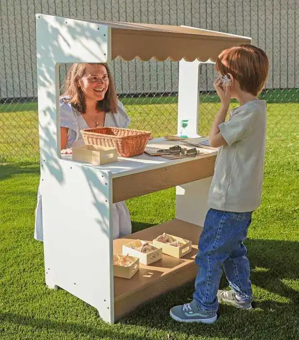 Outdoor wooden market stand with child and teacher engaging in pretend play