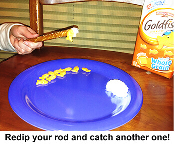 Hand using a pretzel rod with cream cheese on end to pick up goldfish crackers